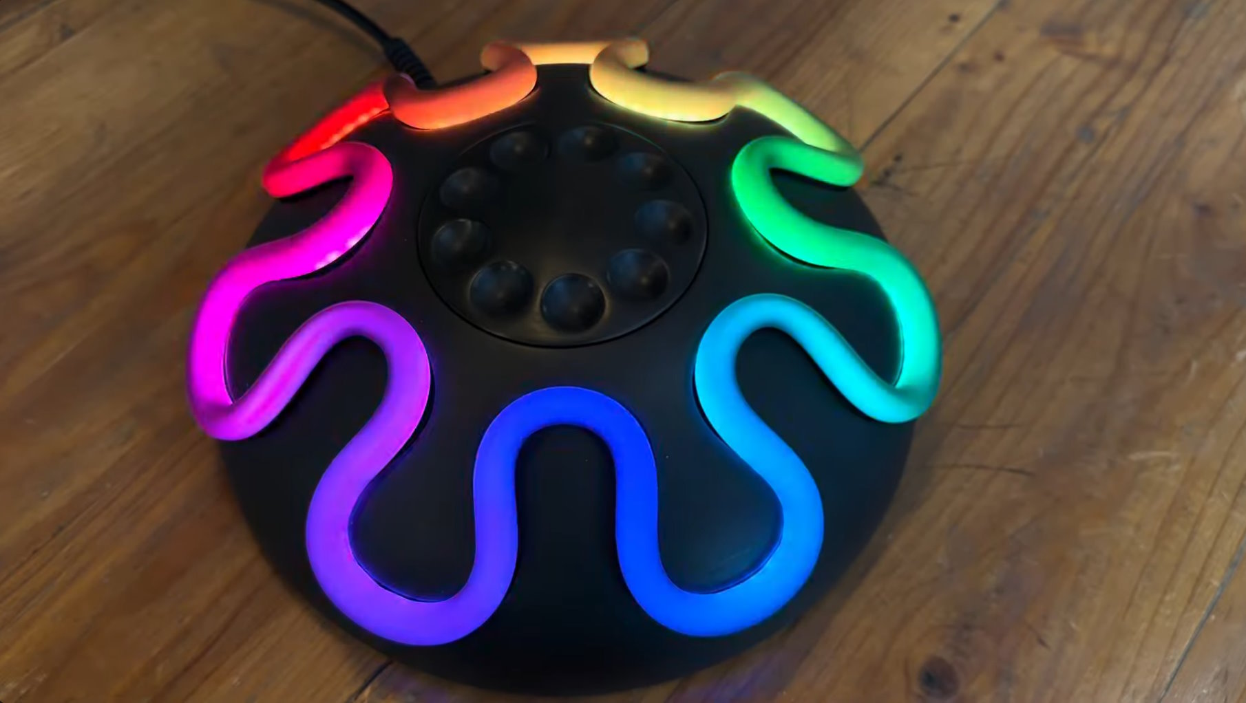 a round black UFO shaped object with a rotary phone like dial on top, and a rainbow coloured stripe of lighting snaking its way back and forth around the edge.